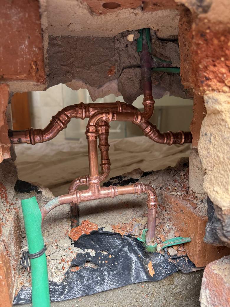 Copper pipework rough-in inside an opened brick wall cavity
